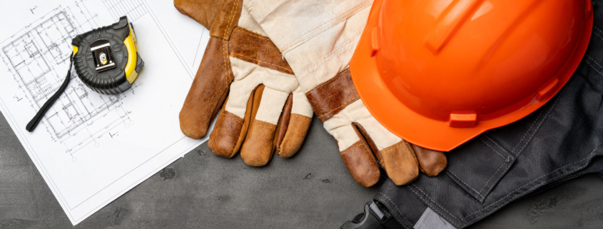 Construction helmet, gloves, and measuring tape on table.